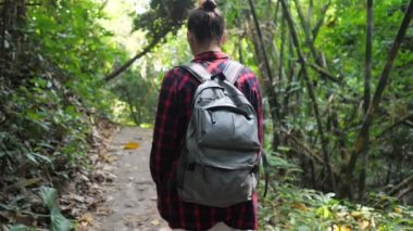Sırt çantalı genç bir kadın yemyeşil tropikal ormanda yürüyor.