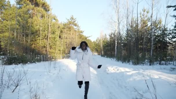 Afroamerikansk flicka springer längs snöig stig i vinterskogen — Stockvideo