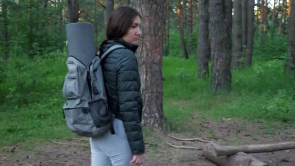 Jonge vrouw in kampeerkleding en met een rugzak stopt in het bos — Stockvideo