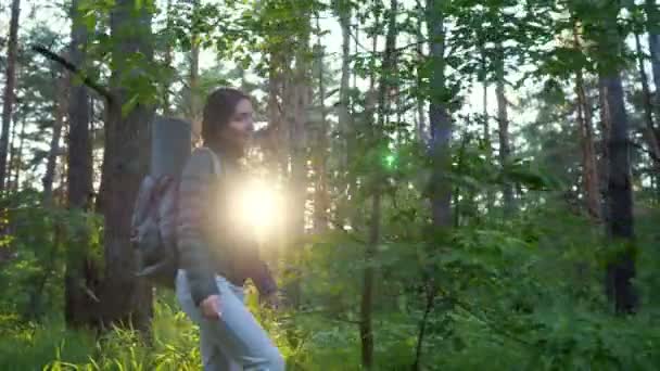 femme avec un sac à dos marche à travers la forêt de conifères sur fond de soleil couchant