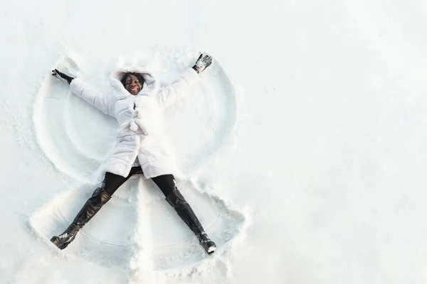 Svart flicka ligger på vit skog glänta och gör snö vinklar — Stockfoto