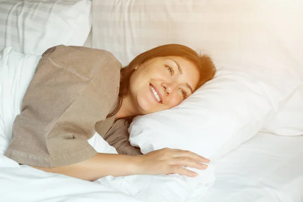 Mujer feliz duerme en la cama con manta y almohadas en el hotel — Foto de Stock