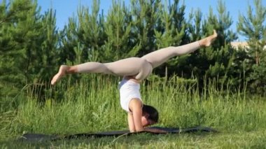 Esmer kadın ellerini jimnastik halısı üzerinde dengeliyor. Yoga dersleri doğada