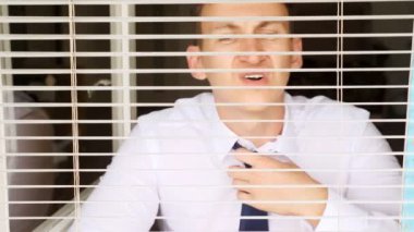 Beyaz gömlekli ve kravatlı bir adam pencerenin önünde panjurlu oturuyor. Oda sıcak ve boğucu.