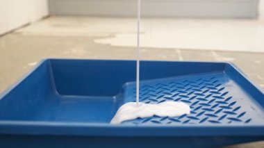 Odadaki mavi plastik tepsiye beyaz boya dökülüyor.