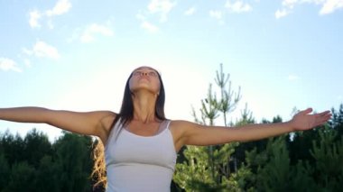 Genç bir kadın, açık havada, güneşli gökyüzünün arka planında yoga yapıyor.