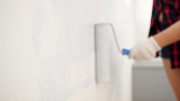 Жінка в рукавичках малює стіну в світло-сірому кольорі з роликом — стокове відео