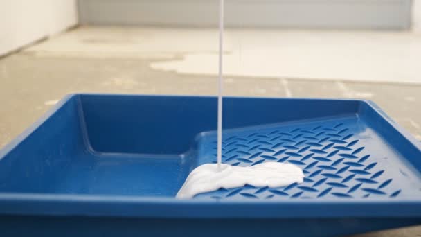 Заливка білої фарби в синій пластиковий лоток на підлозі в кімнаті — стокове відео