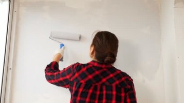 Kareli gömlekli kadın, balkona gri bir duvar çiziyor.