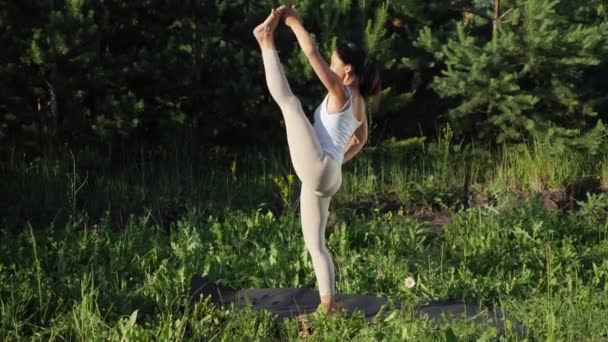 Young woman performs yoga asana standing on one leg outdoors — Stock Video