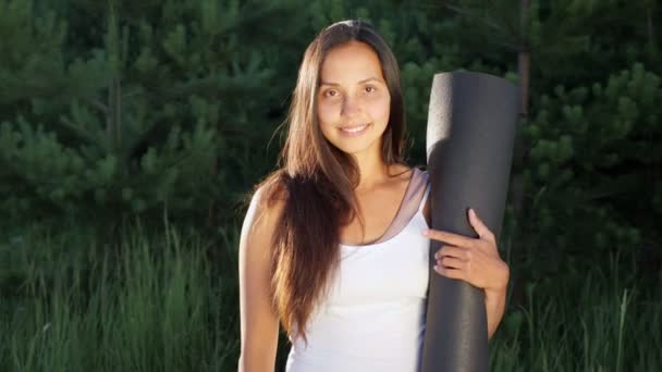 Woman in white t-shirt stands with gymnastic mat and smiles showing thumb up — Stock Video