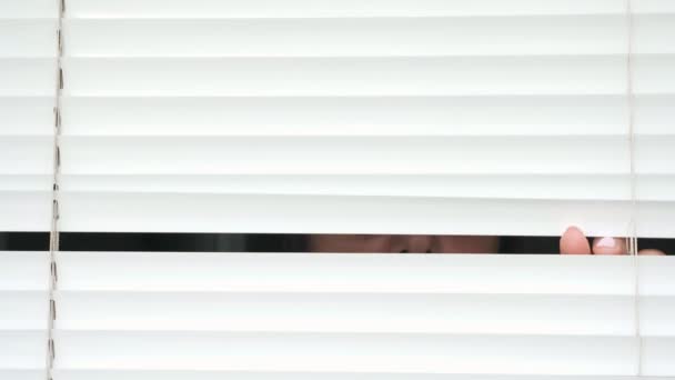 Mulher com óculos olhando para alguém através de persianas brancas — Vídeo de Stock