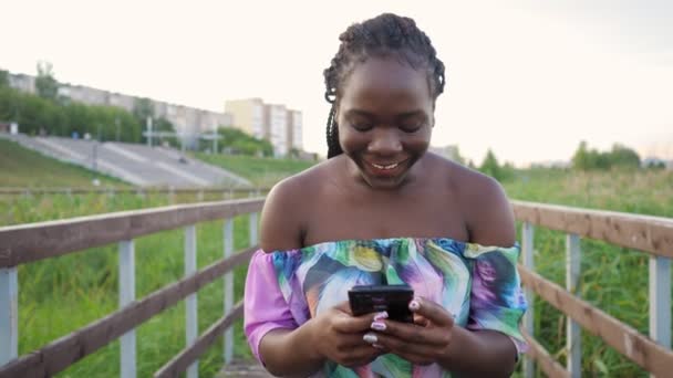 African woman with phone jumping with happiness on wooden bridge — Stock Video