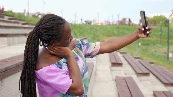 Афроамериканська леді в стильній блузці робить селфі в парку. — стокове відео