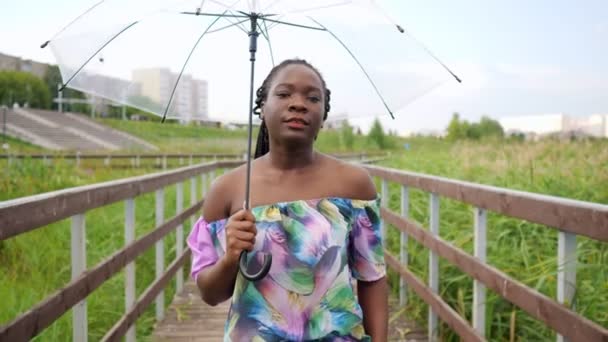 Chica afroamericana con paraguas camina a lo largo del puente — Vídeo de stock