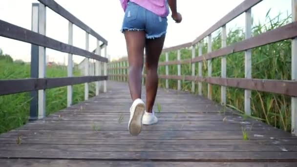 Αφρο-αμερικανική κυρία με μακριά λεπτά πόδια τρέχει κατά μήκος της γέφυρας — Αρχείο Βίντεο