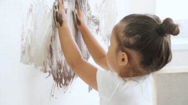 Beyaz tişörtlü çocuk kahverengi boyalı beyaz tuval çiziyor.