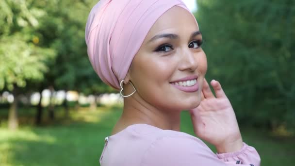 Jovem mulher muçulmana em lenço de cabeça sorrindo no fundo de grama verde e árvores — Vídeo de Stock