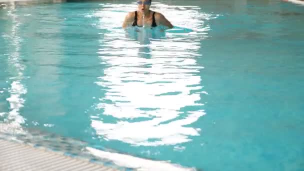 Frau mit schwarzer Mütze schwimmt Brustschwimmen und taucht in Pool — Stockvideo