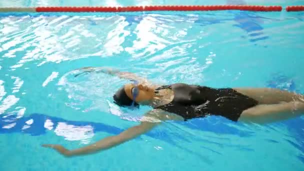 Sportvrouw in zwart swims rugslag stijl in groot zwembad — Stockvideo