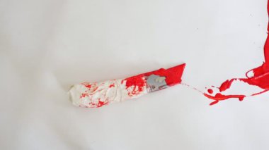 maket bıçağı kırmızı boya damlalarının arasında beyaz arkaplanda yatıyor