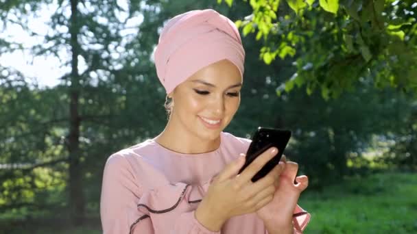 Mulher muçulmana bonita em turbante com telefone no fundo das árvores — Vídeo de Stock