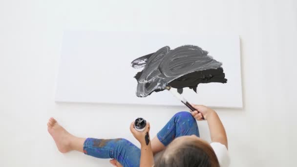 active little girl draws on sheet of paper with black paint
