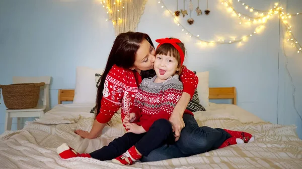 Amorosa madre besa hija contra decoraciones navideñas — Foto de Stock