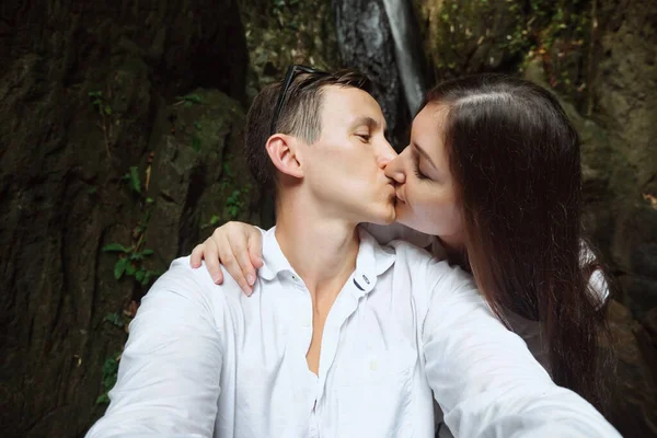 Muž a žena políbit navzájem na pozadí malého vodopádu a skály — Stock fotografie