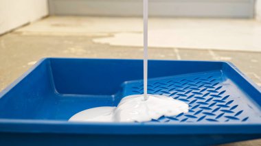 Odadaki mavi plastik tepsiye beyaz boya dökülüyor.