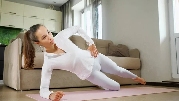 Woman does sports exercises standing in side plank on floor — Stock Photo, Image