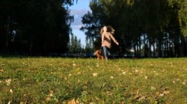 Uzun, dalgalı saçları olan kadın tüylü köpeğin arkasında koşuyor.