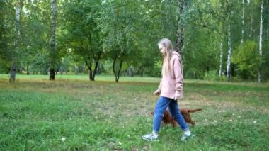 Uzun saçlı kız yeşil parkta komik bir köpekle yürüyor.