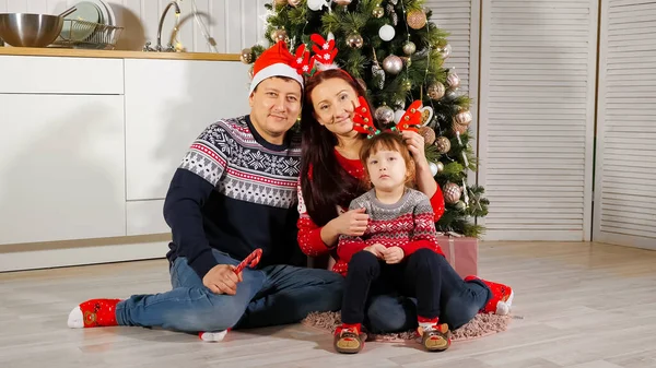 Familia feliz se sienta en el suelo cerca del árbol de Navidad posando en el set — Foto de Stock