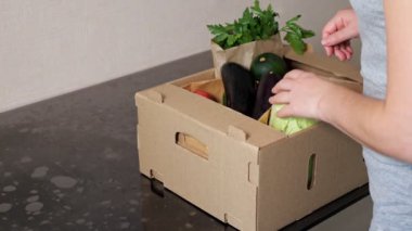 Kadın kahverengi kutuya yaklaşır ve sipariş edilmiş sebzeleri alır.