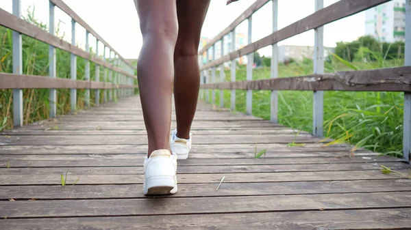 Mujer afroamericana en zapatillas blancas camina a lo largo del puente — Foto de Stock
