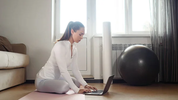 Menina surfa internet com laptop para encontrar exercícios no quarto — Fotografia de Stock