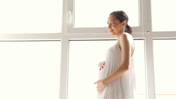 Schwangere im weißen Kleid streicht Bauch nahe Fenster — Stockvideo