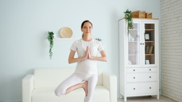 Zwangere vrouw staat in vrksasana in ruime kamer thuis — Stockvideo