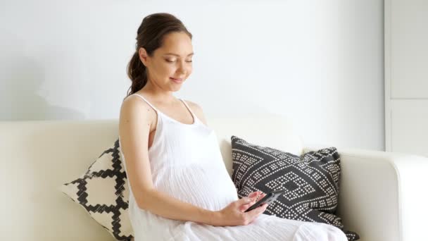 怀孕妇女坐在沙发上，用智能手机上网 — 图库视频影像