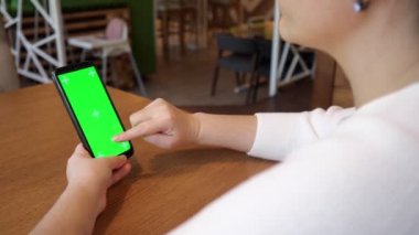 Genç bir kadın yeşil ekran telefonunda parmağını tutuyor.