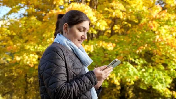 Giovane donna con telefono sullo sfondo di alberi gialli — Video Stock