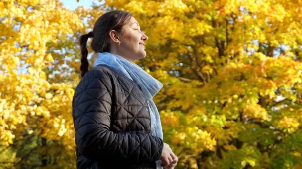 Junge brünette Frau lächelt in die Sonne vor dem Hintergrund gelber Herbstbäume — Stockvideo