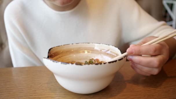 Молодая неузнаваемая женщина ест прозрачную лапшу с морепродуктами в кафе — стоковое видео