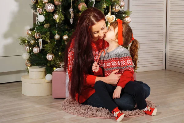 Hijita besando a mamá junto a un árbol de navidad decorado — Foto de Stock
