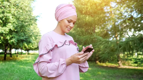 Ung kvinna i lila klänning och hijab typer på smartphone — Stockfoto