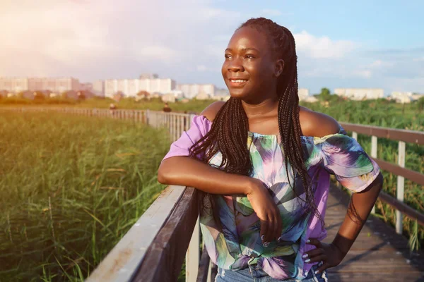 Ung afrikansk amerikansk kvinna lutar sig mot ledstången på bron och tittar bort — Stockfoto