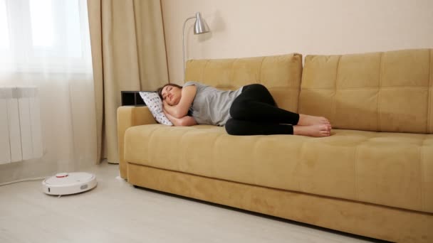 Dame dort sur canapé tandis que robot aspirateurs nettoyeur dans la chambre — Video