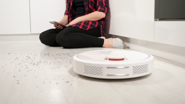 Vrouw met smartphone bestuurt robot stofzuiger thuis — Stockvideo