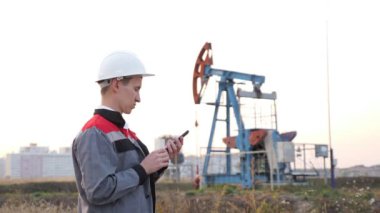 Beyaz kasklı bir adam, bir petrol kuyusunda sallanan arka planda telefonu var.
